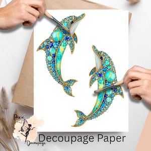 May include: Decoupage paper featuring two bejeweled dolphin designs. The dolphins are adorned with blue and turquoise gemstones, outlined in gold. The paper has the text "Decoupage Paper" at the bottom.
