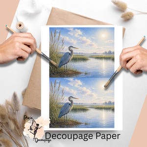 May include: Decoupage paper featuring a serene watercolor painting of a blue heron standing near a body of water, under a bright sun. The paper has the text "Decoupage Paper" and is surrounded by art supplies.
