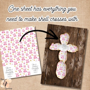 May include: A sheet of paper with a pink teddy bear pattern and a shell cross on a wooden background. The cross has a gold trim and a teddy bear pattern. Text on the paper reads "You are fearfully and wonderfully made."