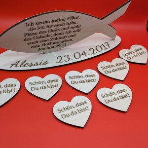 May include: Wooden heart-shaped ornaments with the text "Schön, dass Du da bist!" (German for "It's nice that you are here!") and a wooden fish with the text "Ich kenne meine Pläne, die ich für euch habe, Pläne des Heils und nicht des Unheils; denn ich will euch eine Zukunft und eine Hoffnung geben. Jeremia 29,11" (German for "I know my plans for you, plans for good and not for disaster, to give you a future and a hope." Jeremiah 29:11). The fish is standing on a wooden base with the text "Alessio 23.04.2017".