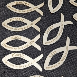 May include: Wooden fish-shaped ornaments with names and the date "04.05.2024" engraved on them. The names include Joschi, Manfred, Norbert, Conny, Edda, Marion, Alicia, Martin, and Werner.