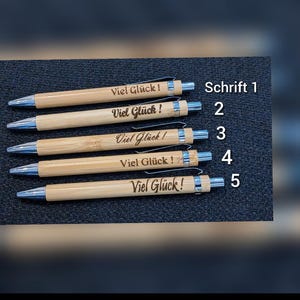 May include: Five bamboo pens with silver accents, each engraved with "Viel Gl&uuml;ck!" in different fonts. The text "Schrift 1-5" is also visible. These pens are ideal for gifting or personal use.