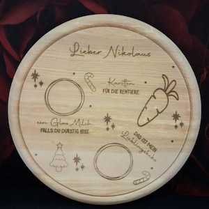 May include: A round wooden plate with a Christmas theme. It has a handwritten message that says "Lieber Nikolaus" and includes images of a candy cane, a carrot, a Christmas tree, and a glass of milk. The text also says "Karotten fur die Rentiere" and "Das ist mein Lieblingskeks".