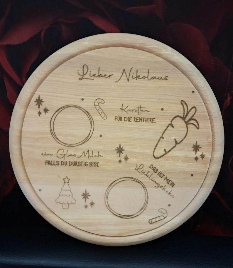 May include: A round wooden plate with a Christmas theme. It has a handwritten message that says "Lieber Nikolaus" and includes images of a candy cane, a carrot, a Christmas tree, and a glass of milk. The text also says "Karotten fur die Rentiere" and "Das ist mein Lieblingskeks".
