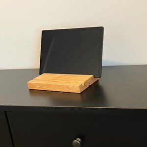 May include: A wooden tablet stand with a natural wood finish. The stand is made of solid wood and has a simple design. It is perfect for propping up a tablet or phone.