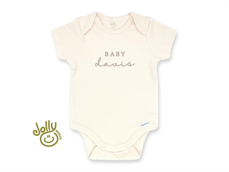 Pu&ograve; includere: Body da bambino color crema con maniche corte e scollo tondo. Il testo "BABY davis" &egrave; stampato in grigio sul petto. Un piccolo logo &egrave; visibile in basso. Il logo Jolly Merch si trova in basso a sinistra.