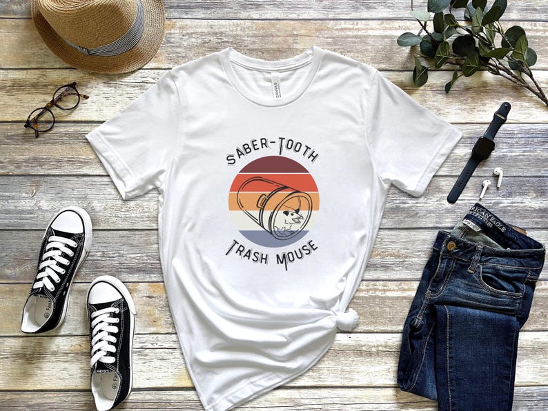 May include: White t-shirt with a retro-style graphic of a trash can with the text "Saber-Tooth Trash Mouse".