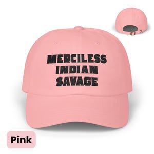 May include: A light pink baseball cap featuring the black embroidered text "MERCILESS INDIAN SAVAGE" on the front panel. The cap has a curved brim and an adjustable strap with a metal buckle at the back, shown in a smaller view in the upper right.
