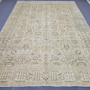 Puede incluir: Gran alfombra beige y marrón estampada. La alfombra presenta un intrincado diseño floral y geométrico con un borde detallado. La paleta de colores es neutra, con tonos beige y marrón, creando una estética vintage o antigua.
