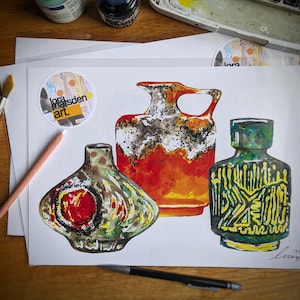 Może przedstawiać: Trzy ceramiczne wazony w różnych stylach i kolorach. Największy wazon jest pomarańczowy i biały z pstrokatą glazurą. Środkowy wazon jest zielony i żółty z geometrycznym wzorem. Najmniejszy wazon jest zielony i brązowy z czerwonym kołem w środku.