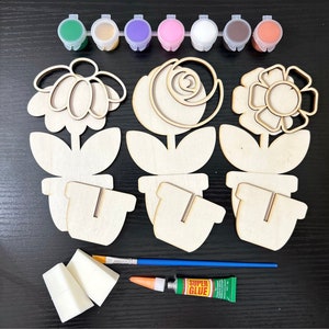 May include: A set of three wooden flower pot craft kits with paint, glue, and brushes. The flowers are in the shapes of a daisy, rose, and a simple flower.