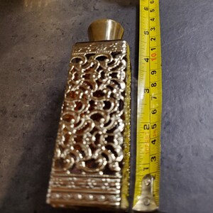 May include: A gold and amber glass perfume bottle with a decorative, intricate design. The bottle is approximately 6 inches tall.