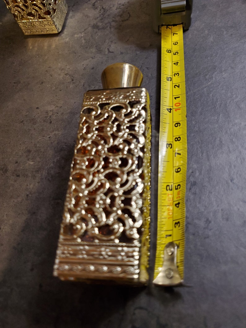 May include: A gold and amber glass perfume bottle with a decorative, intricate design. The bottle is approximately 6 inches tall.