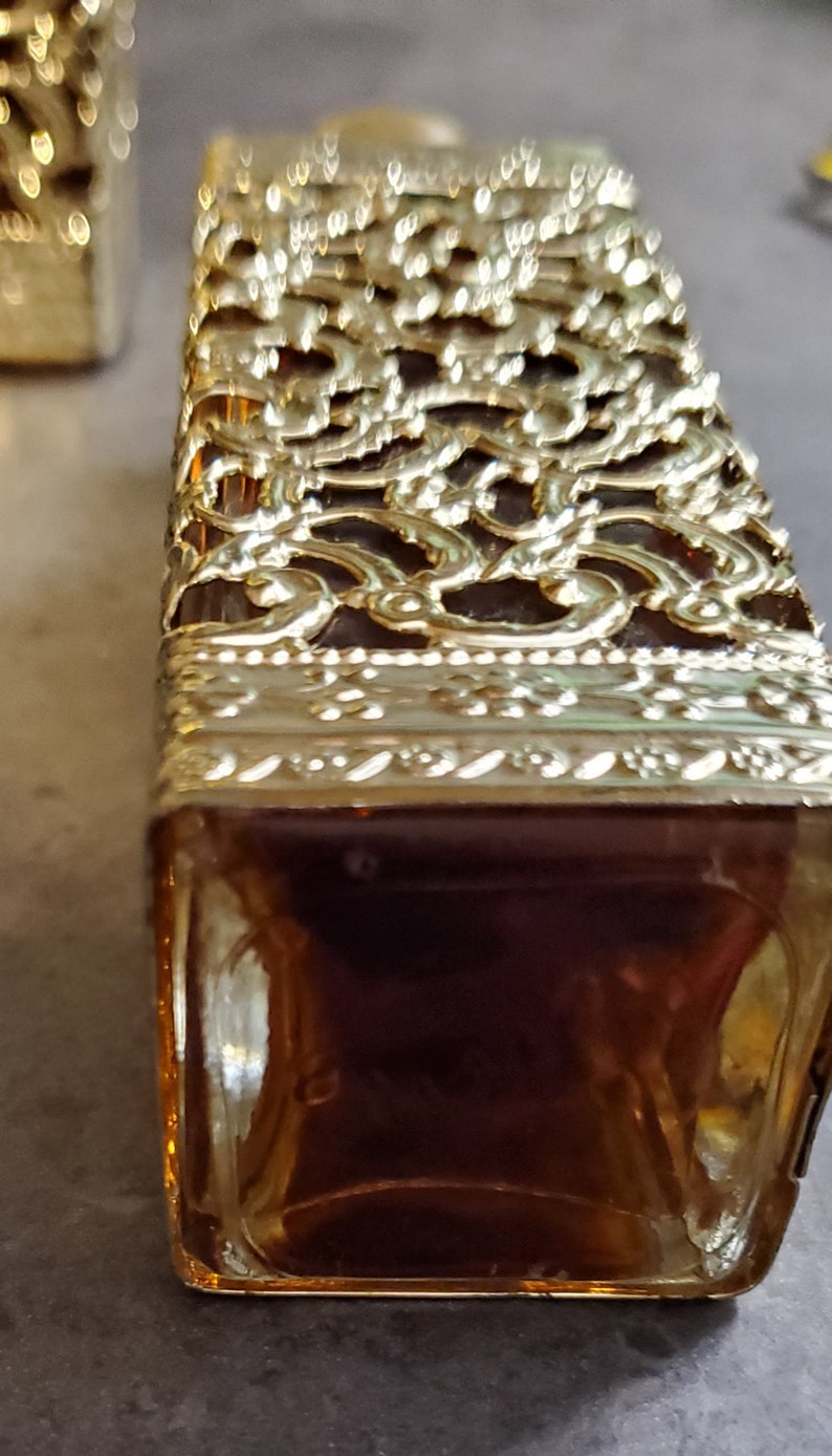 May include: A gold-colored glass bottle with a decorative, intricate design. The bottle is filled with a dark liquid.