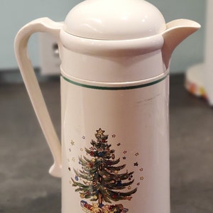 May include: White ceramic thermal carafe with a green trim and a Christmas tree design. The tree is decorated with ornaments, stars, and presents.