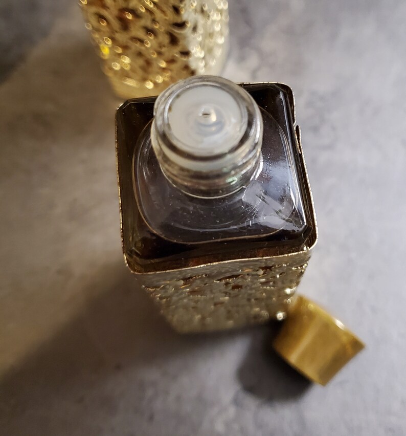 May include: A gold-colored glass bottle with a clear glass stopper. The bottle has a textured surface and is filled with a dark liquid.