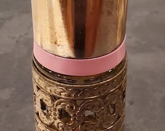May include: A vintage perfume bottle with a gold-colored metal top and filigree design on the lower portion. A pink band encircles the bottle near the top of the filigree. The bottle is cylindrical.