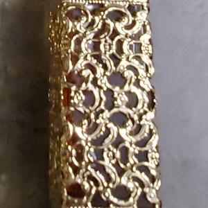 May include: A gold decorative bottle with a detailed filigree design. The bottle is clear glass and has a gold cap.