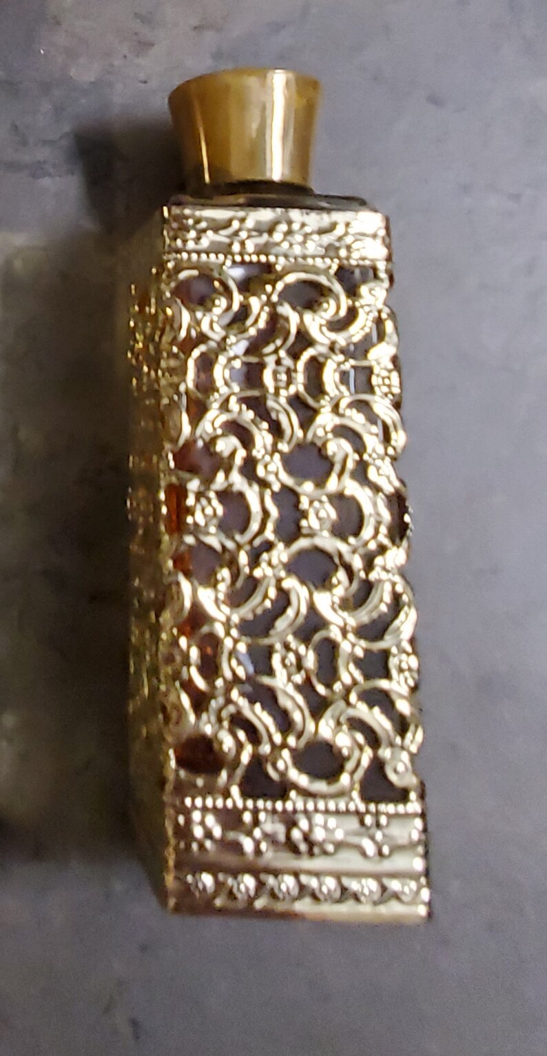 May include: A gold decorative bottle with a detailed filigree design. The bottle is clear glass and has a gold cap.