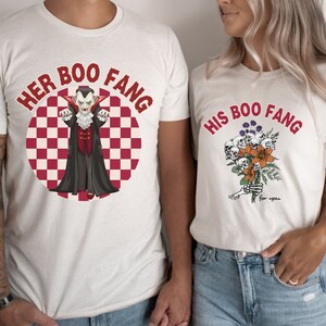 May include: Two white t-shirts with a red and white checkered background. One shirt says "Her Boo Fang" with a cartoon vampire. The other shirt says "His Boo Fang" with a bouquet of skulls and flowers.