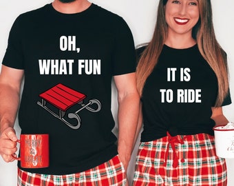 Puede incluir: Una pareja lleva camisetas negras a juego con un tema navideño. La camiseta del hombre dice "Oh, What Fun" con un gráfico de trineo rojo. La camiseta de la mujer dice "It Is To Ride". Ambos llevan pantalones de pijama de cuadros rojos y verdes.