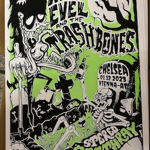 May include: A black and white illustration of a cartoon monster with green slime and a skeleton holding a guitar. The text "Wild Evel and the Trashbones" is at the top of the poster. The text "Chelsea 01.12.2023 Vienna-AT" is on a tombstone. The text "Stereo Deathray" is at the bottom of the poster.