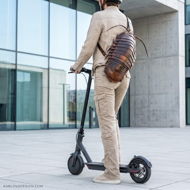 May include: A brown, segmented, insect-shaped backpack with long antennae worn on the back. The backpack features a hard, layered shell design resembling a giant isopod. The text KARLOVADESIGN.COM is visible in the bottom left corner of the image.