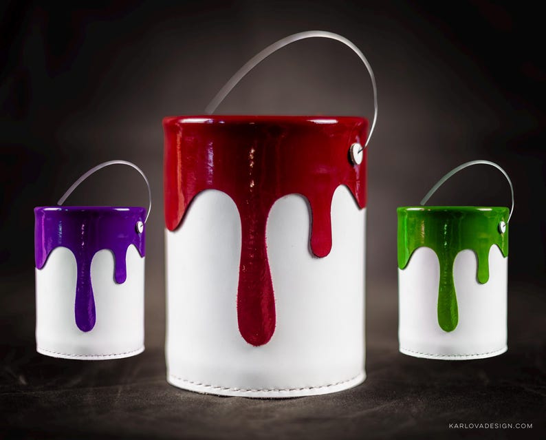 Peut inclure: Trois contenants en forme de pot de peinture avec des poign&eacute;es. Les contenants sont blancs avec de la peinture rouge, violette et verte qui coule sur les c&ocirc;t&eacute;s.