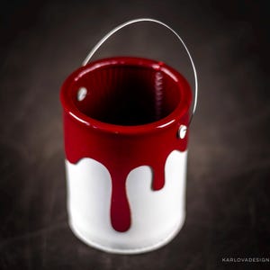 Peut inclure: Un petit pot de peinture blanc avec un couvercle en m&eacute;tal rouge et une coul&eacute;e de peinture rouge sur le c&ocirc;t&eacute;. Le pot a une poign&eacute;e en fil d'argent.