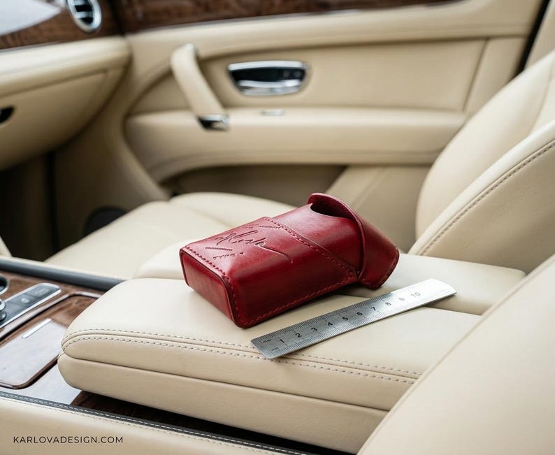 May include: A deep red leather case with a flap closure and a debossed signature logo on the front. A silver metal ruler is placed next to the case, showing a length of approximately 10 cm for the item. The case has visible stitching.