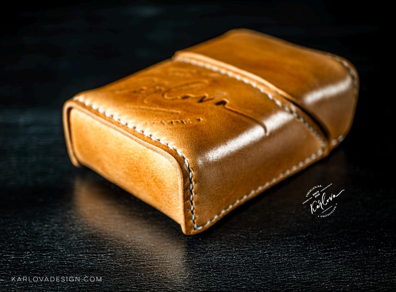 May include: A tan leather case with a hinged lid and visible white stitching along the edges. The surface features an embossed script logo that reads Karlova, with additional text reading Original Since 2018 Karlova Products and Karlovadesign.com.