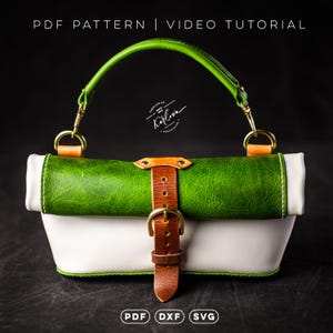 May include: A handmade leather handbag with a green and white color scheme. The bag features a brown leather strap with a buckle closure and a green handle. The text "PDF PATTERN | VIDEO TUTORIAL" is at the top.