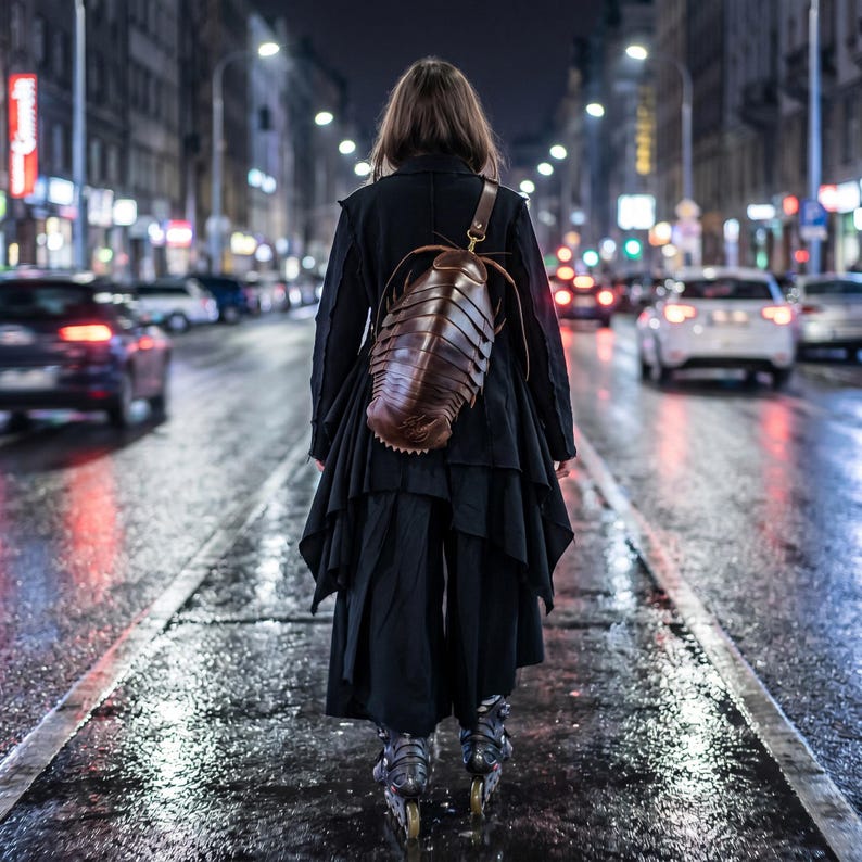 May include: A brown leather backpack shaped like a large cockroach with segmented body details and a single shoulder strap, worn over a black layered jacket and black trousers, with inline skates visible at the bottom of the frame.