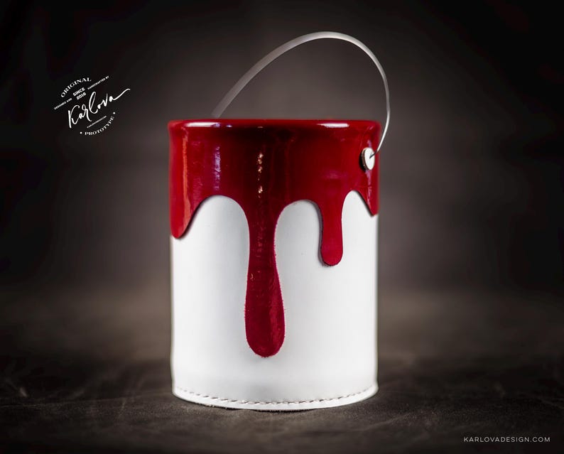 Peut inclure: Un pot de peinture blanc avec un couvercle rouge et de la peinture rouge qui coule sur le c&ocirc;t&eacute;. Le pot a une poign&eacute;e en m&eacute;tal.