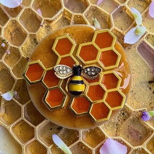 May include: A decorative bee-themed item featuring a golden honeycomb design with a yellow and black bee. The bee has crystal accents on its wings. The item is set on a honeycomb-patterned surface.