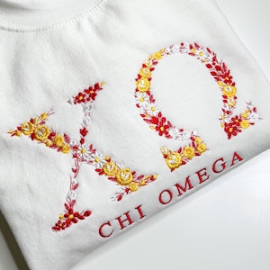 May include: White t-shirt with embroidered floral letters "ΧΩ" and the text "CHI OMEGA" in red.