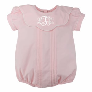 May include: A light pink baby romper with a Peter Pan collar and short sleeves. The collar and sleeve edges are trimmed with white piping. The front features vertical pleats and a white monogram.
