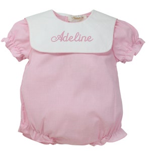 May include: Pink and white gingham baby onesie with a white sailor collar and the name "Adeline" embroidered on the collar.