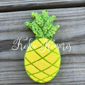 May include: A green glitter pineapple with a yellow body and a green outline. The pineapple is on a wooden background.