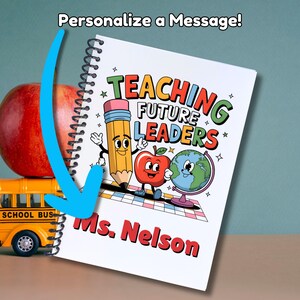 May include: A white spiral notebook with a colorful illustration of a pencil, apple, and globe. The text "Teaching Future Leaders" is in a colorful retro font. The notebook is personalized with the name "Ms. Nelson".