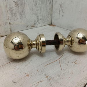 May include: A pair of polished brass door knobs with a round, spherical design. The knobs are connected by a metal rod.