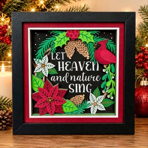 May include: A square black shadow box frame containing a layered paper art piece. The design features a red cardinal, green holly leaves, white and red poinsettias, and pinecones. The text reads, Let heaven and nature sing, in white.