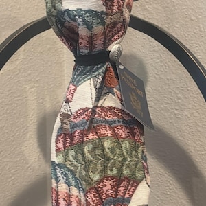 May include: A decorative wine bottle bag with a colorful hot air balloon pattern. The bag is tied with a black ribbon and a silver button. A tag that says "Wine Passport" is attached.