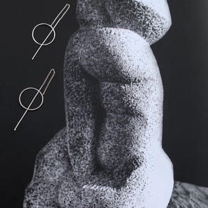 Pode incluir: Um par de brincos de prata com um círculo e uma linha reta. Os brincos são exibidos contra um fundo preto com uma escultura branca.
