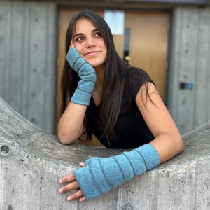 May include: A person wearing a blue fingerless arm warmer on both arms. The arm warmers are made of a soft, textured fabric. The person is wearing a black shirt and has long dark hair.