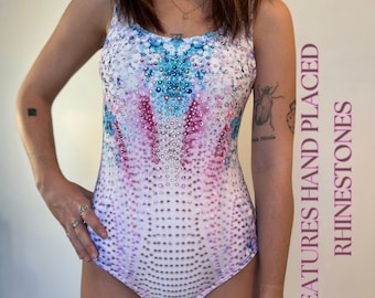Könnte beinhalten: Ein Badeanzug mit farbenfrohem, abstraktem Design. Der Badeanzug hat handversetzte Strasssteine und ein Muster aus blauen, rosa und weißen Farbtönen. Der Text auf der Seite lautet "FEATURES HAND PLACED RHINESTONES".