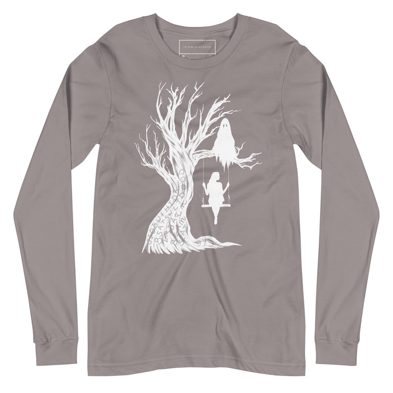 May include: A long-sleeved t-shirt in a heather grey color with a white graphic design of a tree with a ghost and a person on a swing. The tree has words written on it.