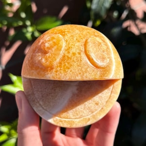 Puede incluir: Una escultura tallada en piedra naranja y blanca de una cara sonriente. La escultura está hecha de dos mitades que encajan.