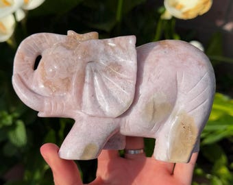 May include: A hand holds a pink carved elephant figurine. The elephant is made of a smooth, polished stone.