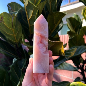 May include: A pink and white crystal point with a swirling pattern. The crystal is about 6 inches tall and is held in a hand.